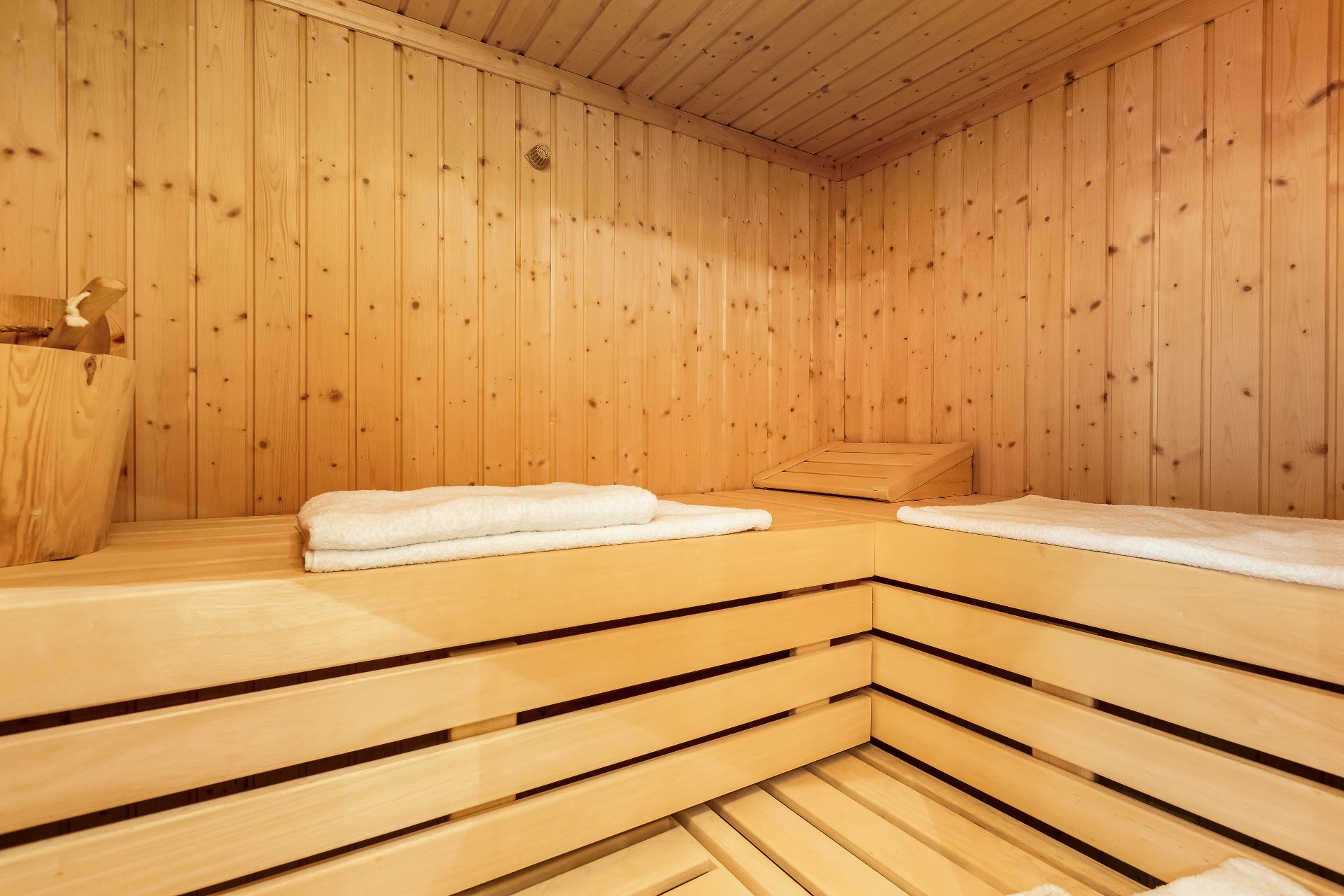 Helle Holzsauna mit Sitzbänken, weißen Handtüchern und einem Eimer auf der linken Seite.