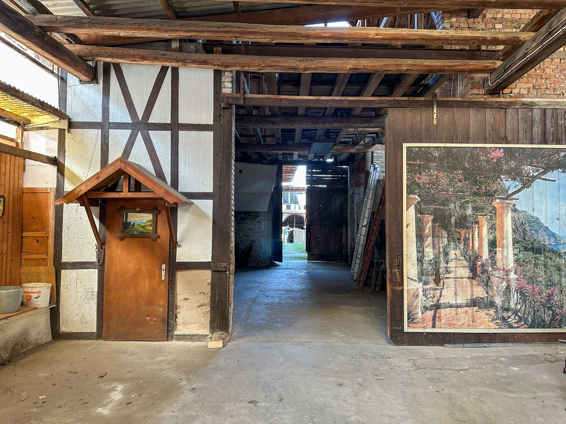 Innenhof mit Holztür, gemalter Szene an der Wand und offenem Durchgang nach draußen.
