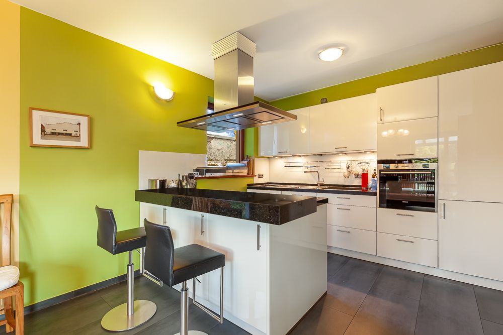 Moderne Küche mit grüner Wand, weißem Schrank, Insel und zwei Barhockern.