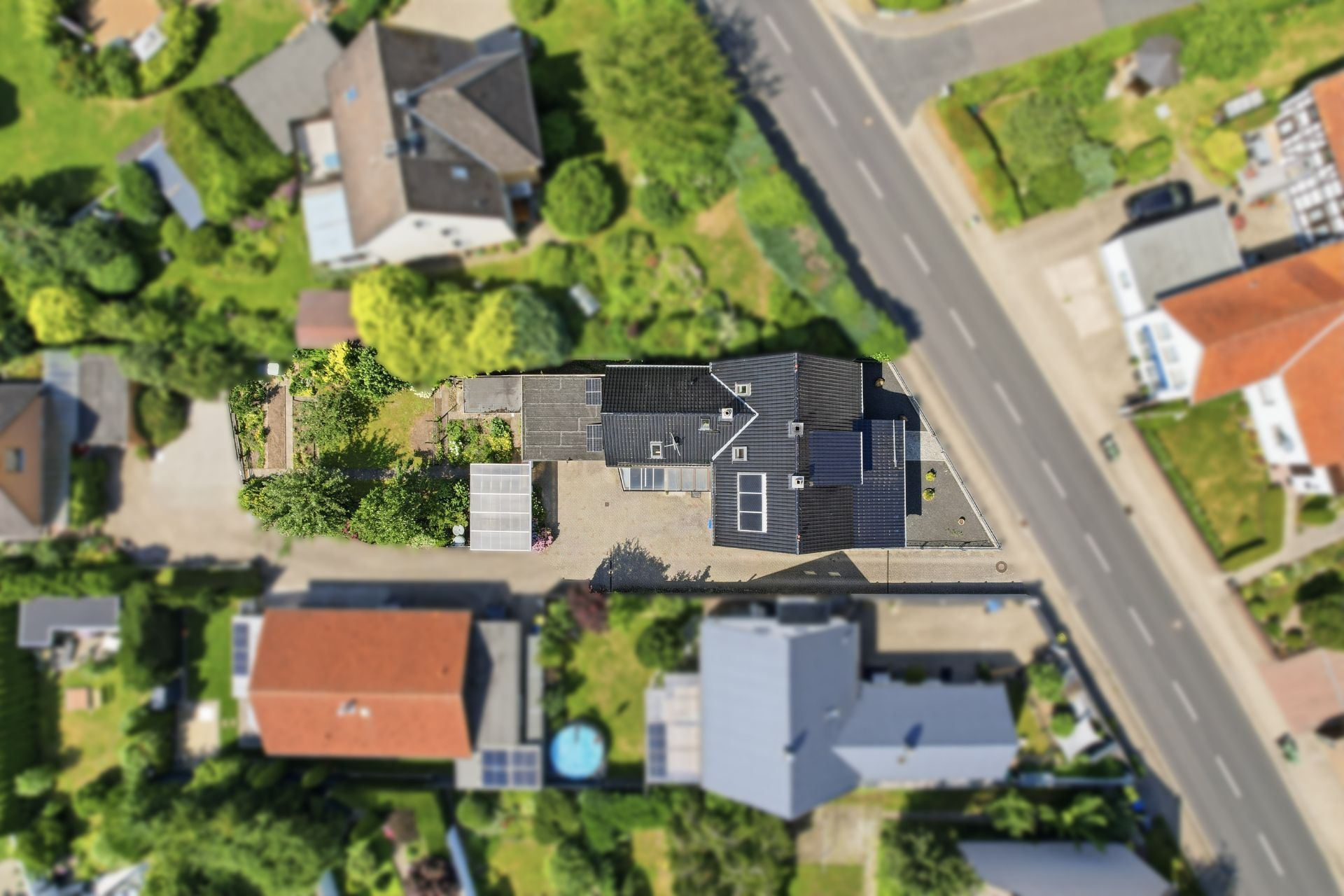 Luftaufnahme eines Wohnhauses mit Garten, Einfahrt und umliegenden Grundstücken an einer Straße.