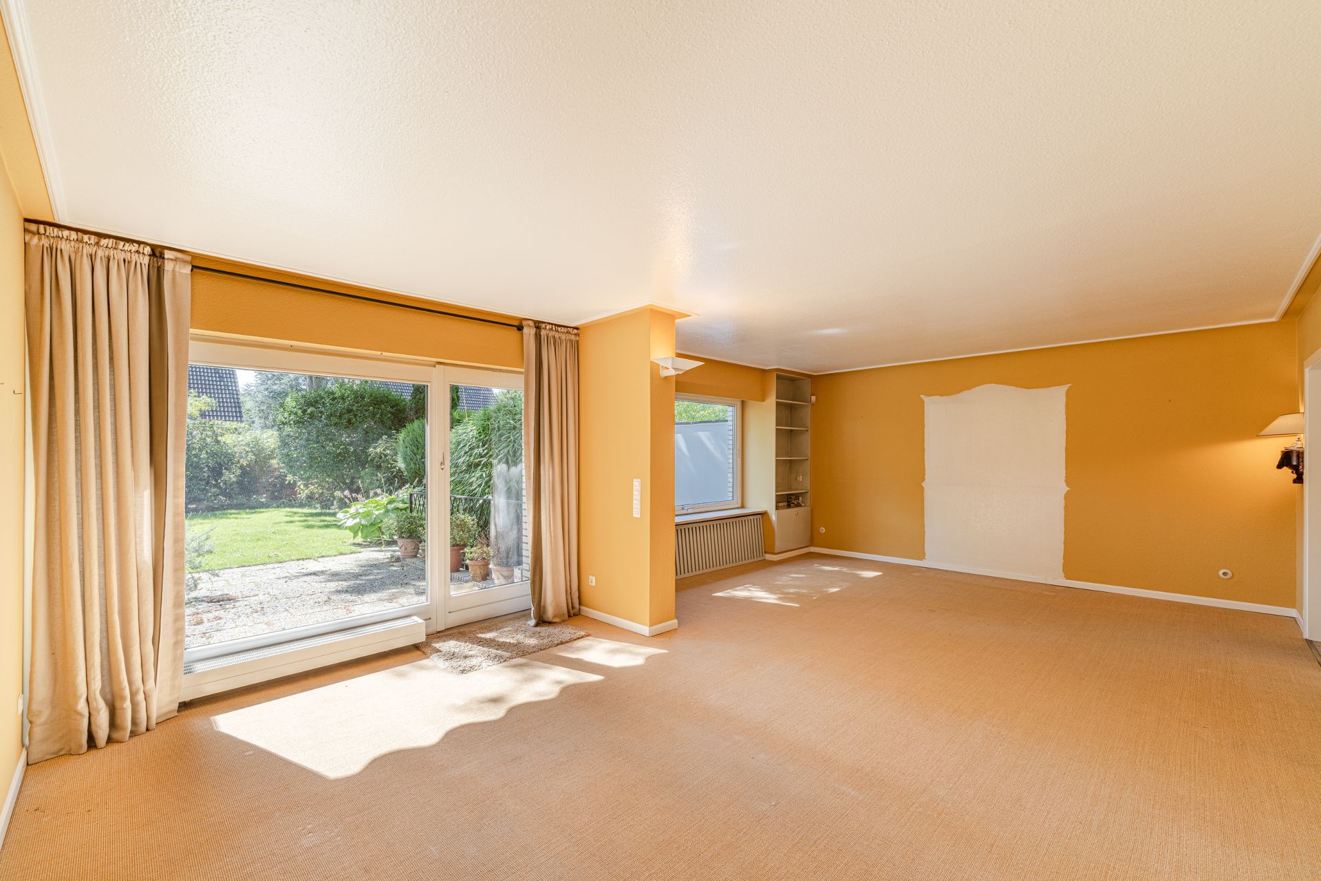 Helles Wohnzimmer mit großen Fenstern, gelben Wänden und Blick auf den Garten.