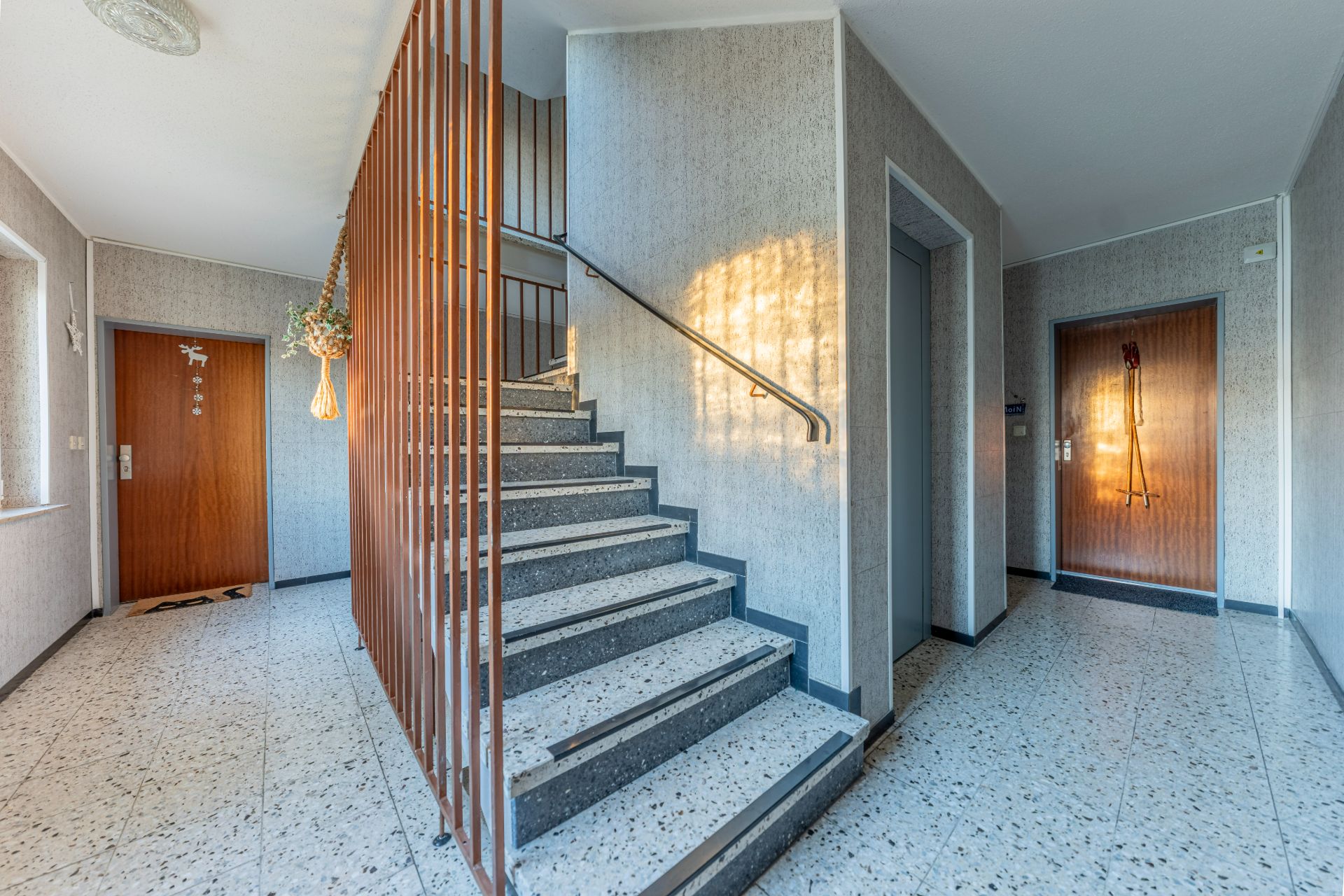 Heller Treppenhausflur mit zwei Wohnungstüren, Aufzug und Fenster.