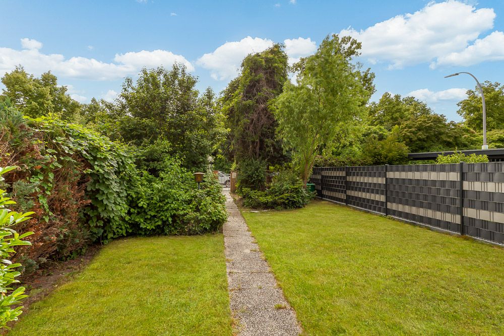 Garten mit Rasenfläche, Weg aus Betonplatten und vielen Bäumen und Sträuchern.