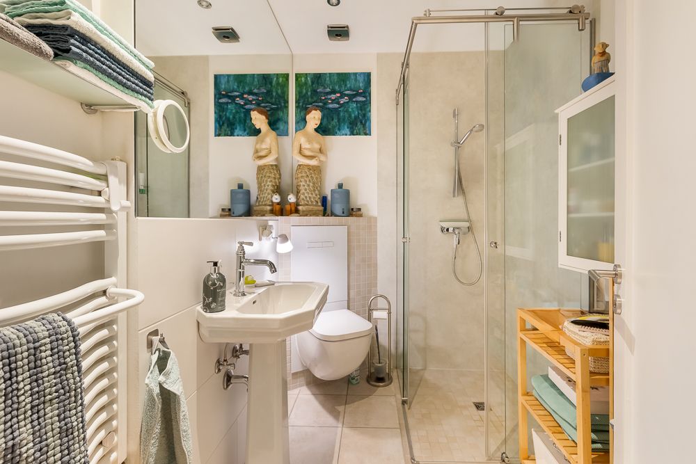 Modernes Badezimmer mit Dusche, Wandtoilette, Waschbecken und Handtuchheizkörper.