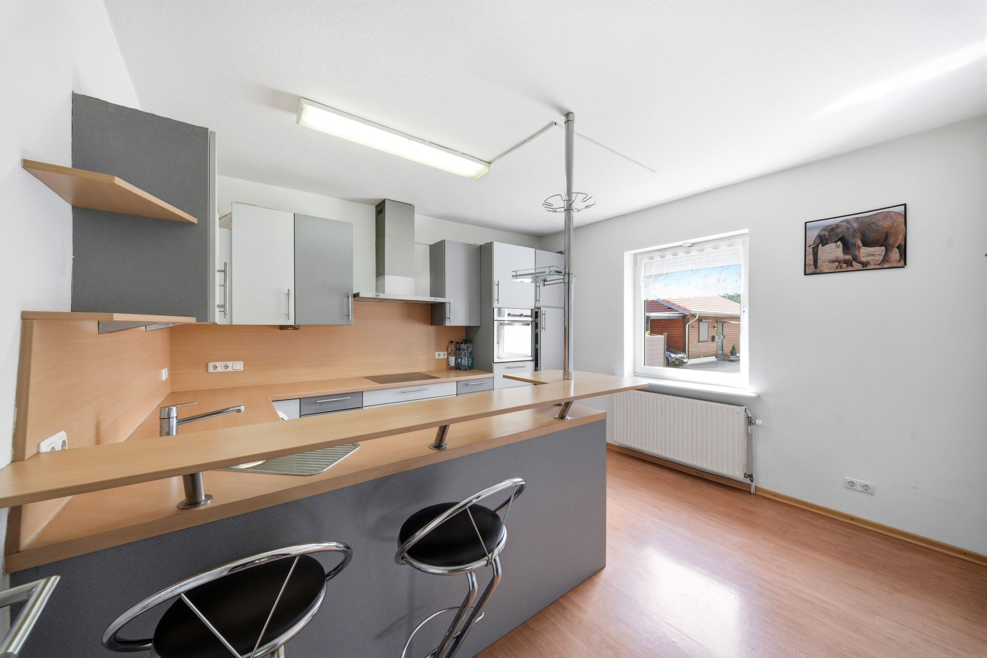 Moderne Einbauküche mit Tresen und zwei Barhockern in einem hellen Raum mit Fenster.