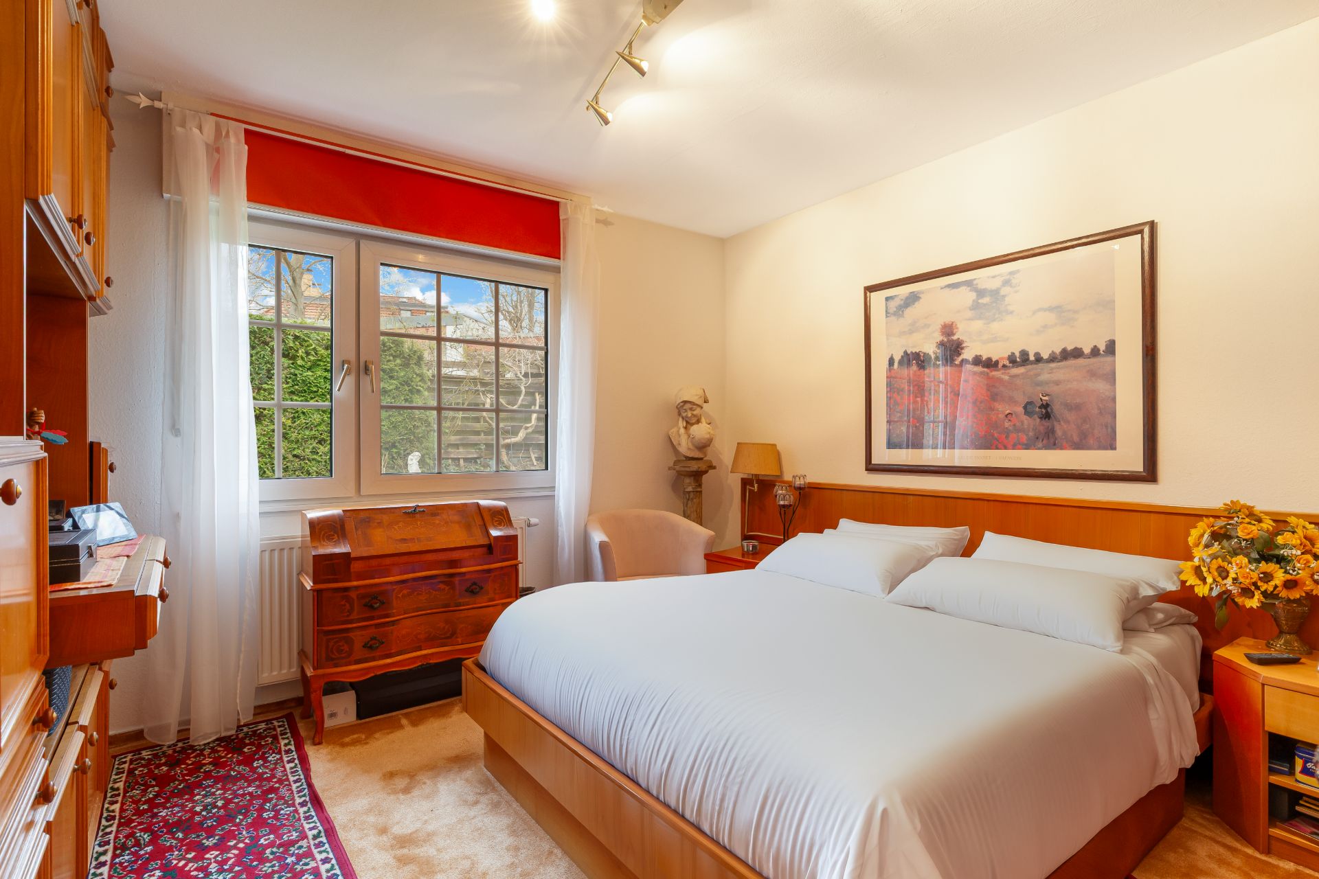 Helles Schlafzimmer mit großem Bett, Holzmöbeln, Fenster und Wandbild.
