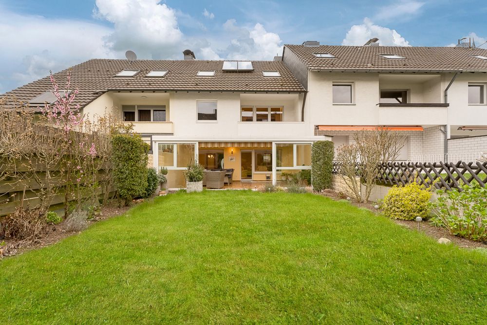 Reihenhaus mit Terrasse und gepflegtem Garten, Hecken und Blumenbeeten im Vordergrund.