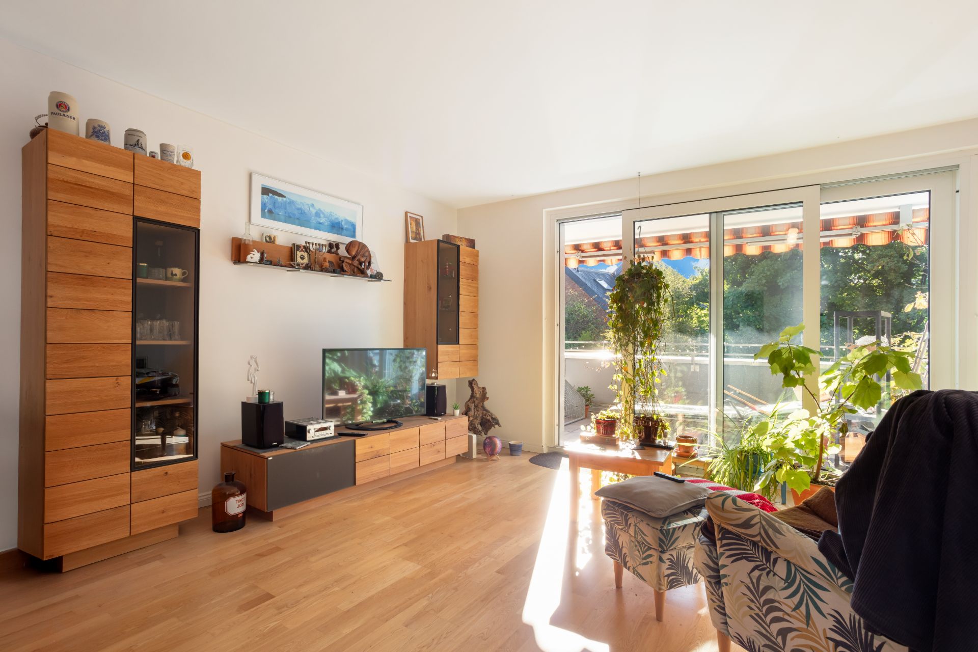 Helles Wohnzimmer mit Holzboden, großen Fenstern, Pflanzen und modernen Holzmöbeln.