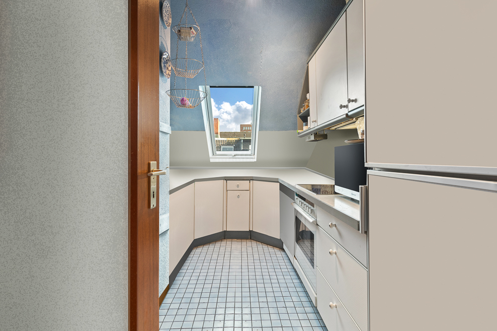 Helle Küche mit Dachschräge, Fenster, weißen Schränken und Fliesenboden.