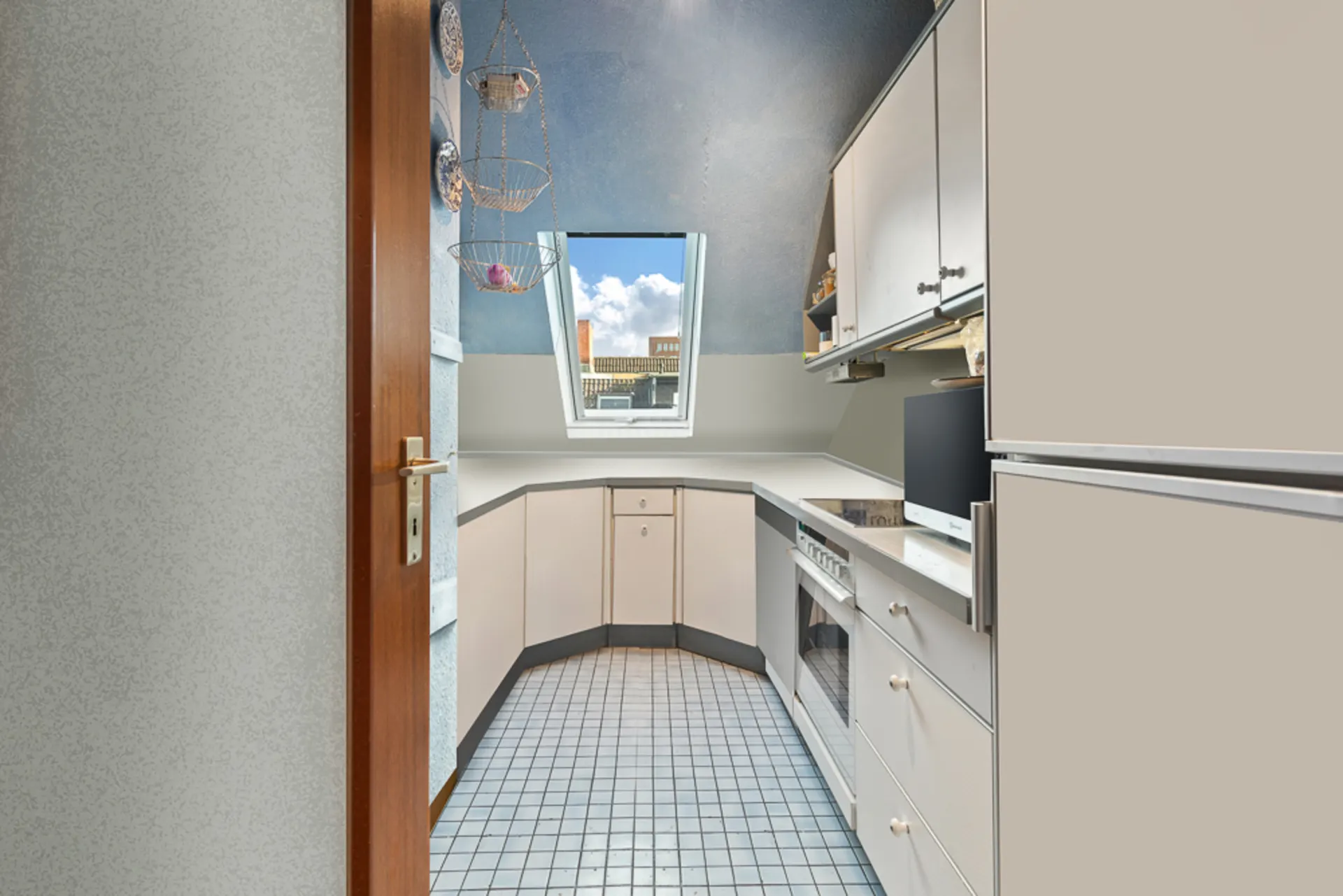 Helle Küche mit Dachschräge, Fenster, weißen Schränken und Fliesenboden.