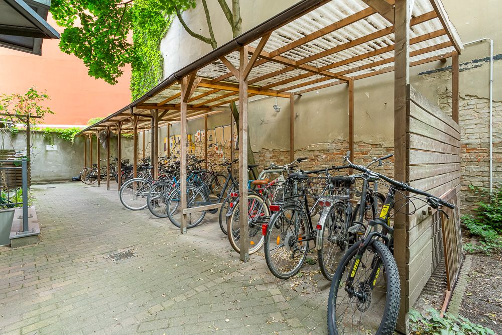 Überdachter Fahrradabstellplatz mit mehreren Fahrrädern neben einer Mauer im Innenhof.