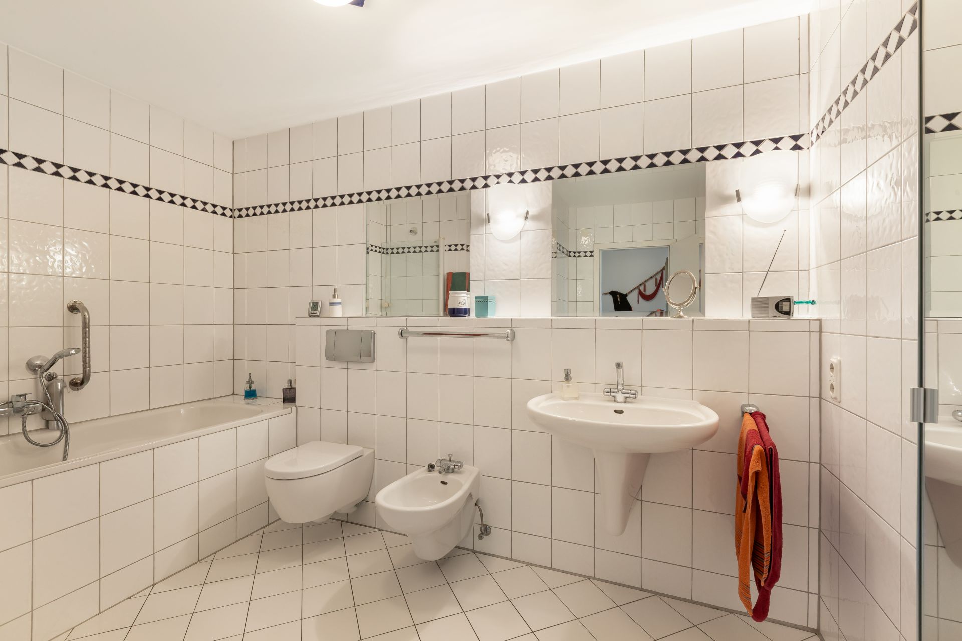 Helles Badezimmer mit Badewanne, WC, Bidet, Waschbecken und großem Spiegel, weiße Fliesenwände.