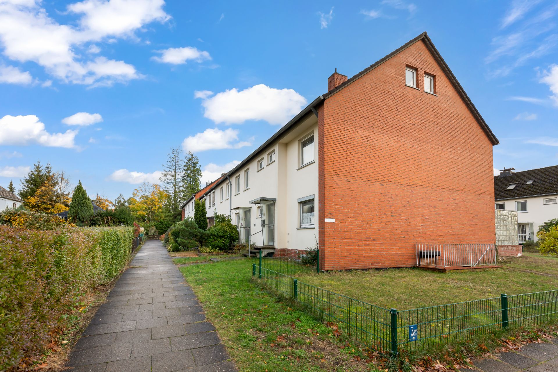 Reihenhaus mit roter Giebelseite und Garten neben einem Gehweg.