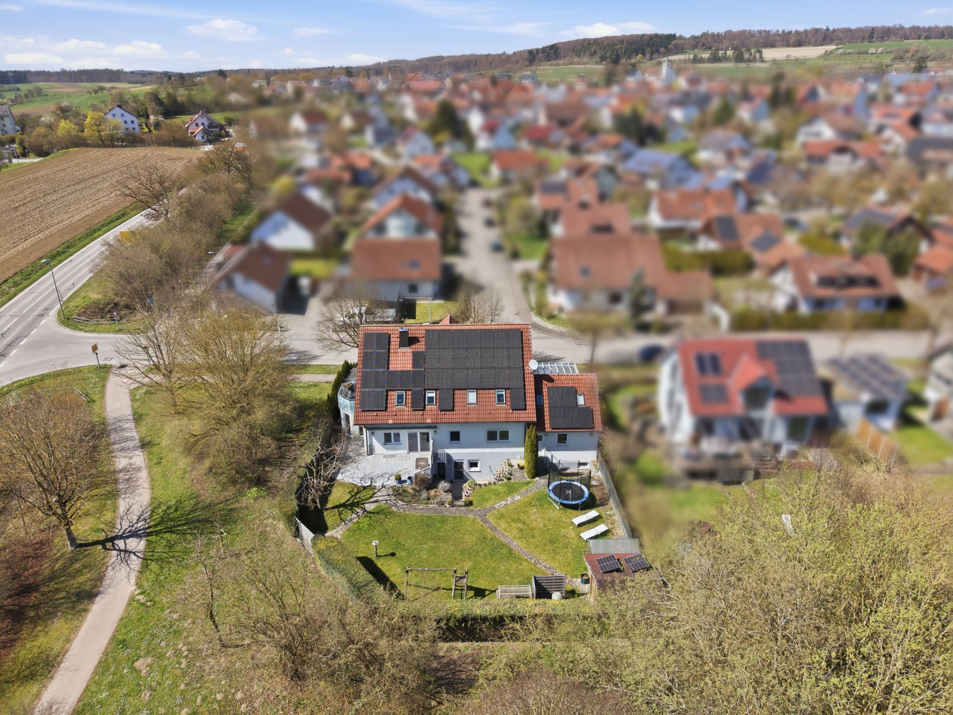 Luftaufnahme eines Wohnhauses mit Garten, Solarpanels auf dem Dach und umliegenden Häusern.