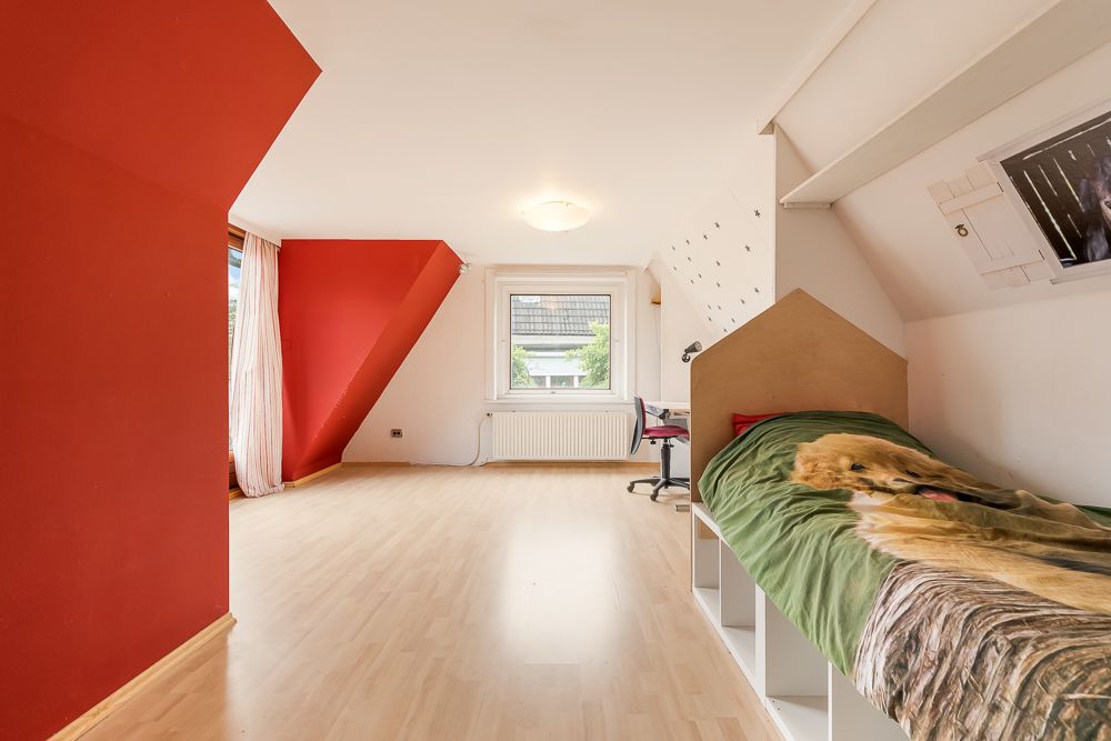 Heller Raum mit roter Wand, Einzelbett, Schreibtisch und großem Fenster.
