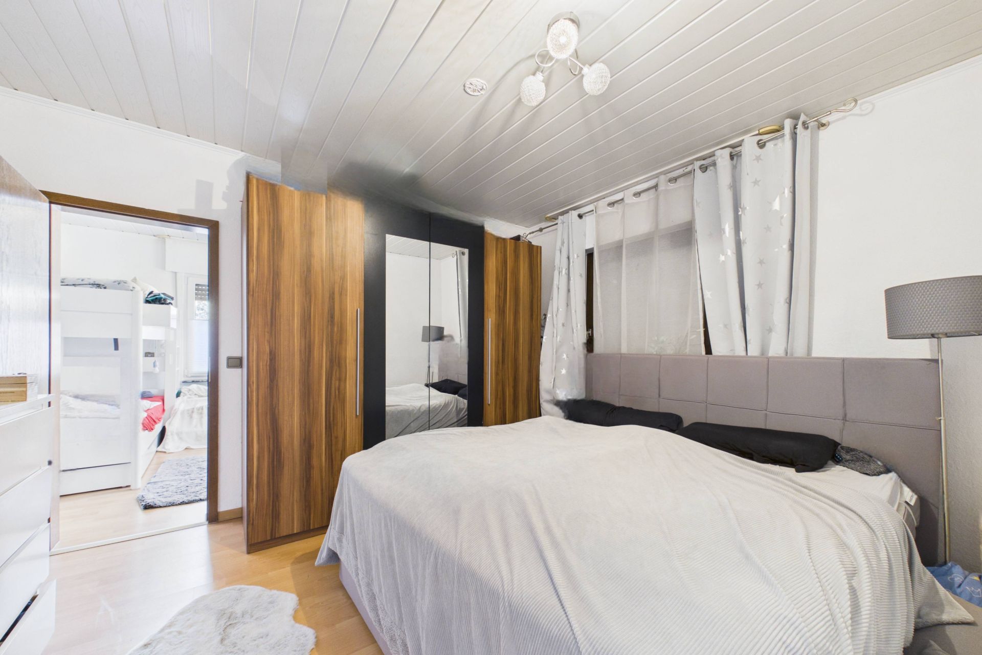 Schlafzimmer mit Doppelbett, Kleiderschrank mit Spiegel und Stehlampe neben dem Bett.