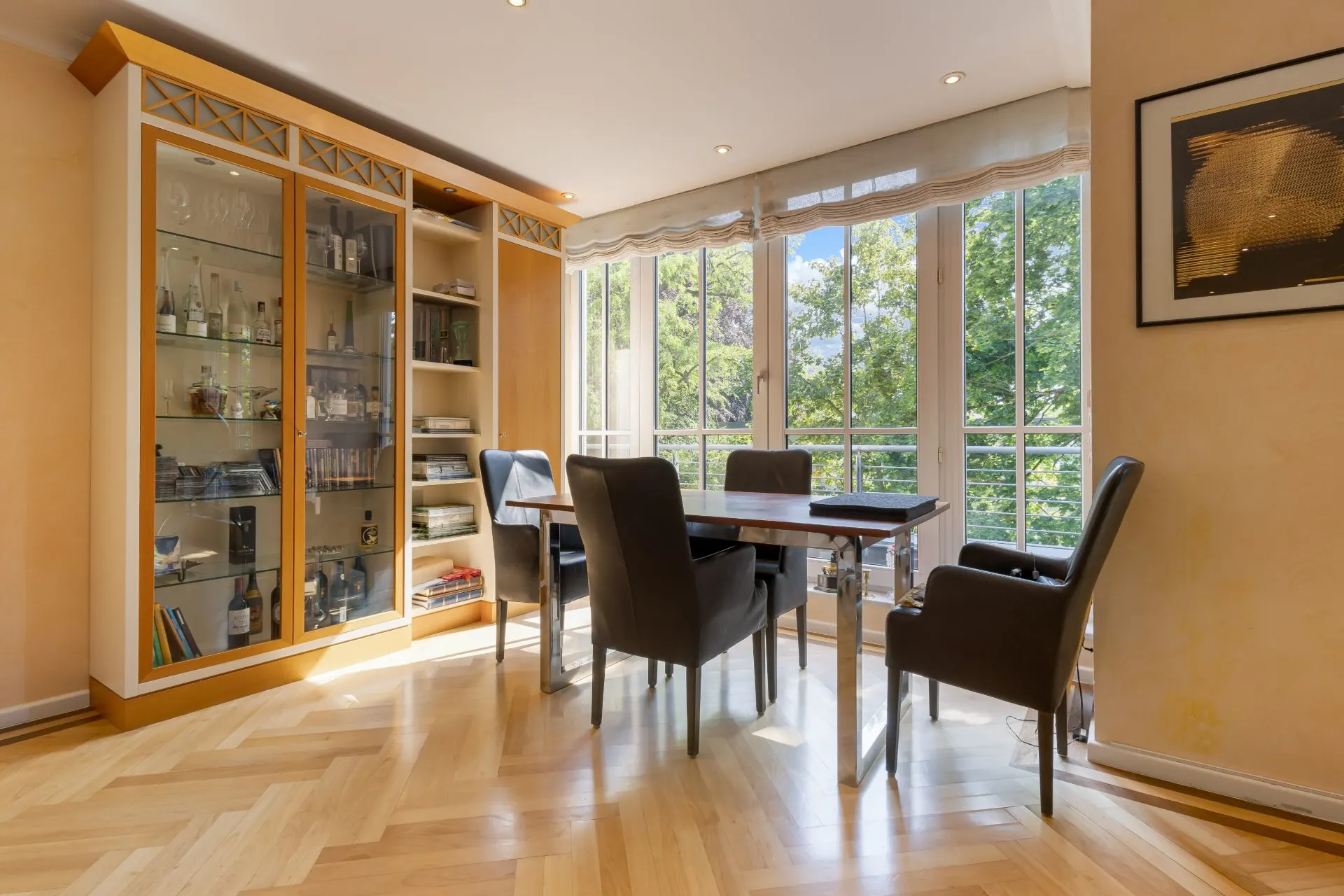 Essbereich mit vier Stühlen, Holztisch, Glasvitrine und großen Fenstern mit Blick ins Grüne.