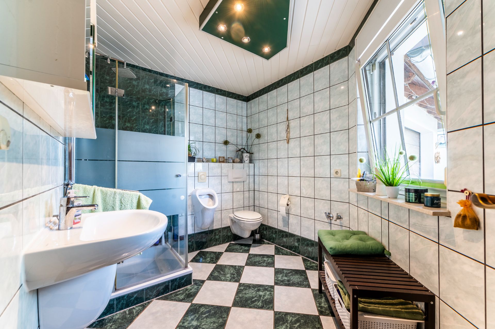 Helles Badezimmer mit Dusche, WC, Waschbecken, Fenster und gemustertem Fliesenboden.