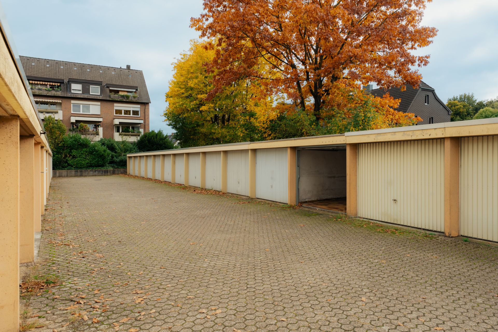 Reihe von Garagen mit offenen Toren auf gepflastertem Hof, im Hintergrund Bäume und Wohnhäuser.