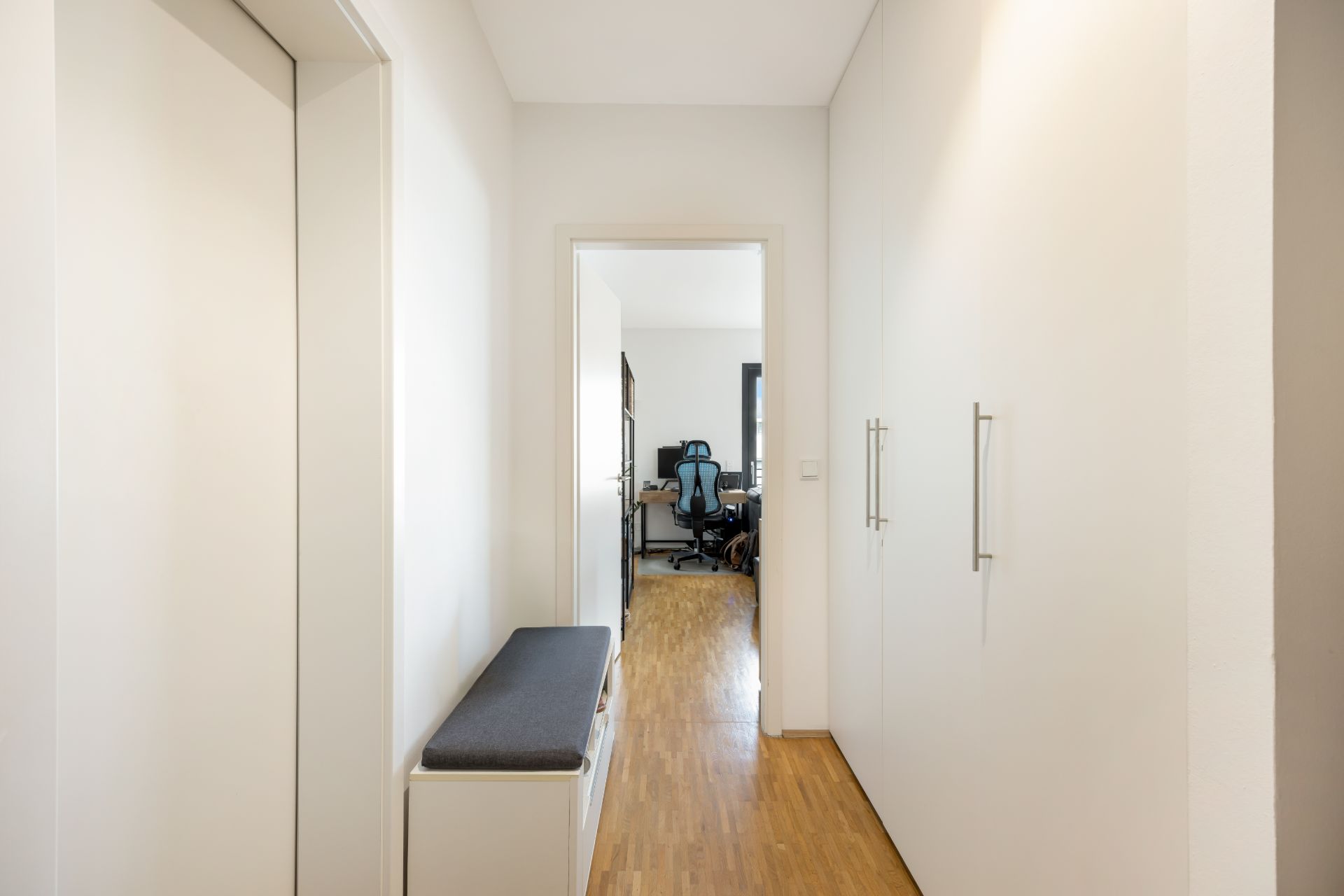 Heller Flur mit Sitzbank und weißen Einbauschränken, Blick in ein Arbeitszimmer mit Schreibtisch und Stuhl.