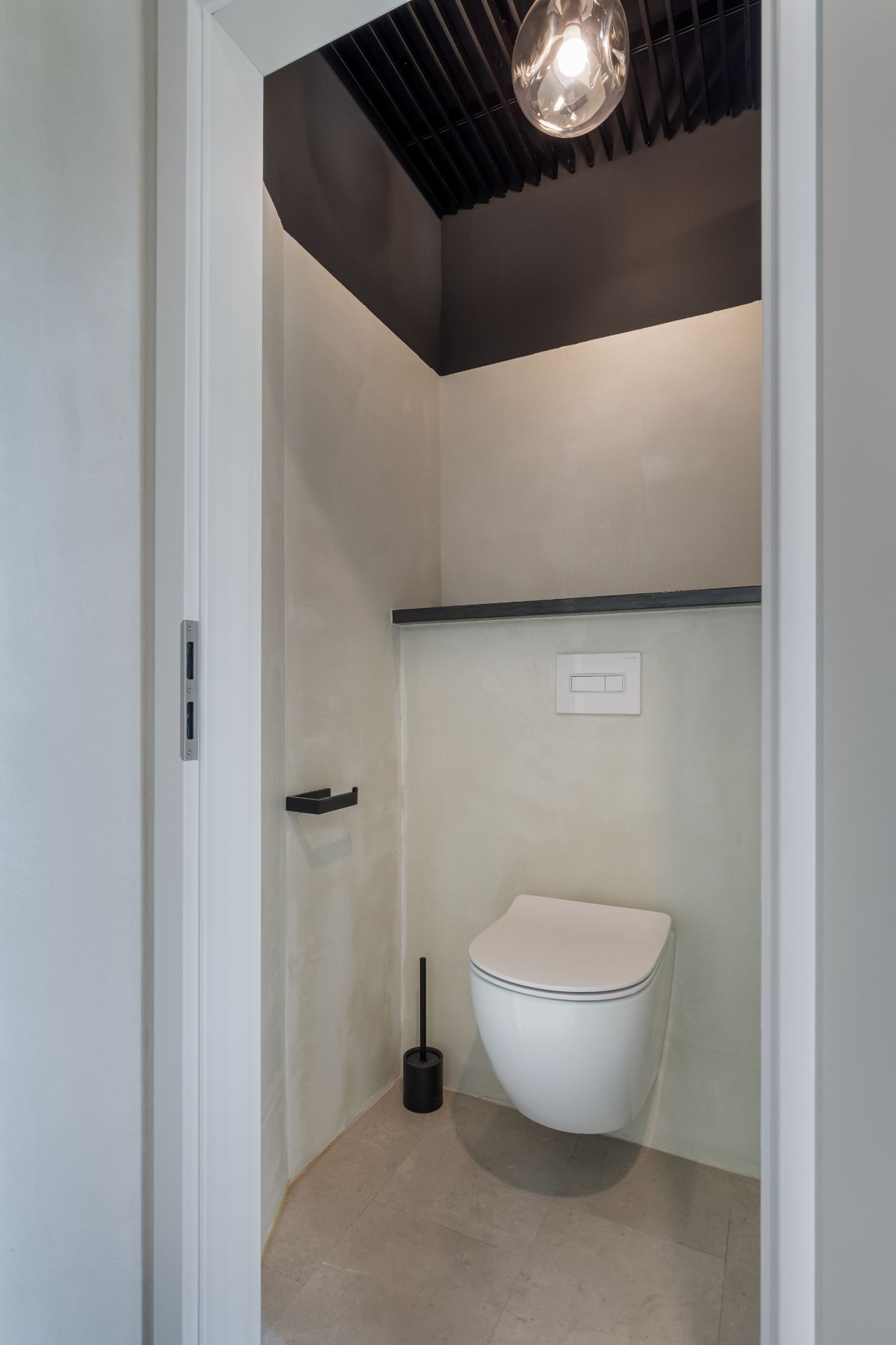 Kleines Badezimmer mit Wandtoilette, Toilettenbürste und schwarzem Regal.