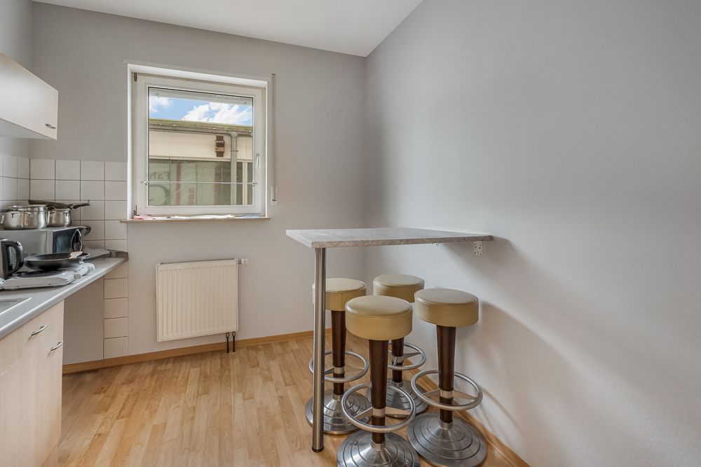Kleine Küche mit Fenster, Bartisch und vier Barhockern auf Holzfußboden.