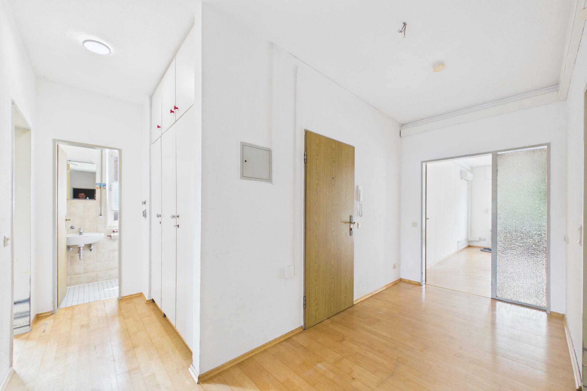 Heller Flur mit Holzboden, weißen Wänden, Türen zu Badezimmer und Zimmer, Einbauschränken.