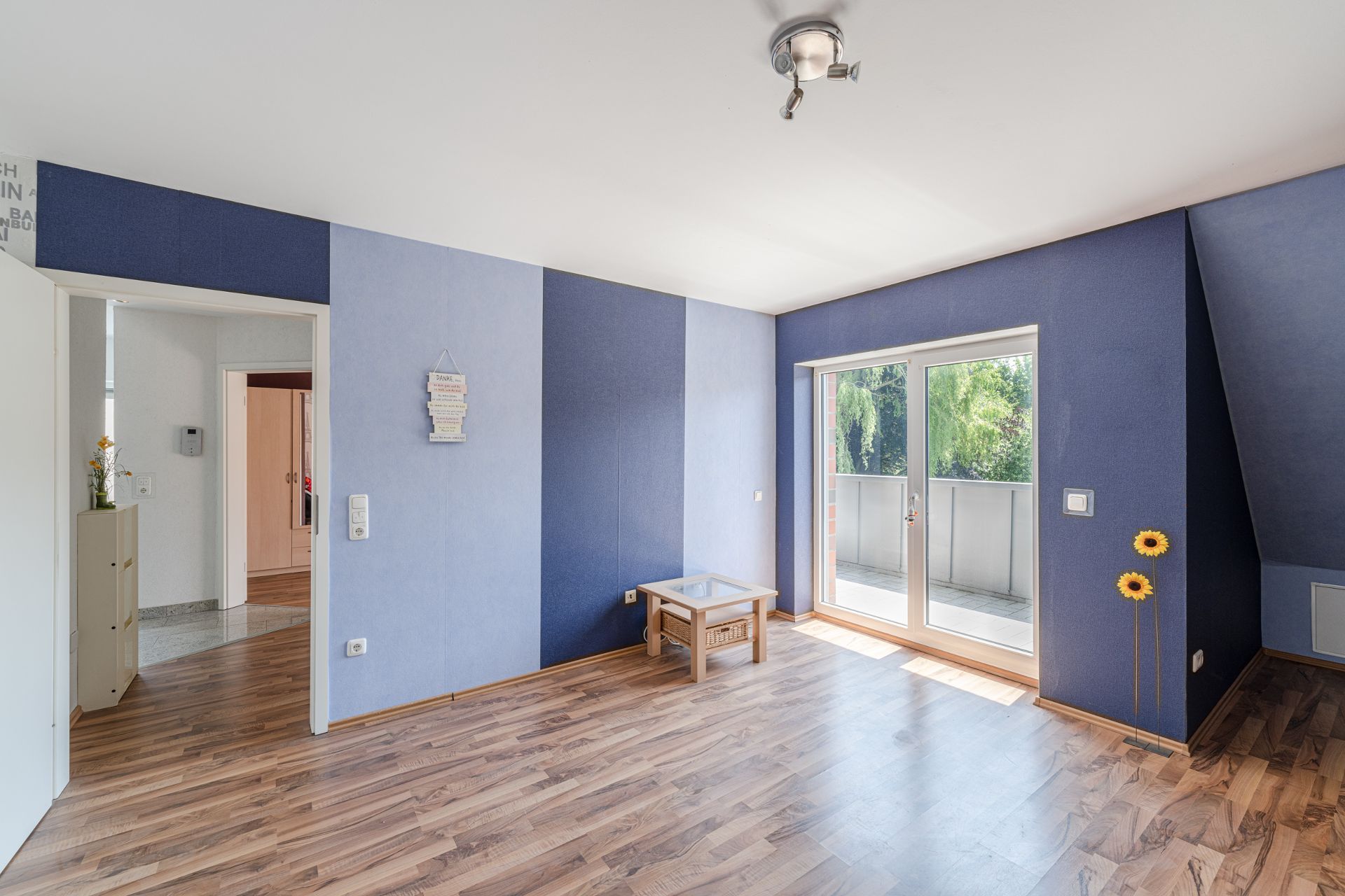 Helles Zimmer mit Holzboden, blauen Wänden, kleinem Tisch und Zugang zum Balkon.