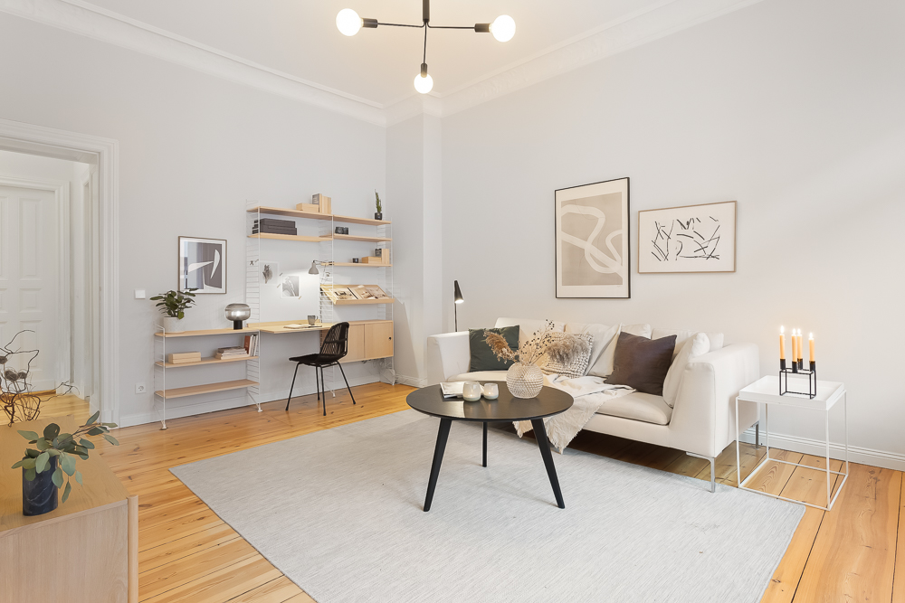 Helles Wohnzimmer mit Sofa, Couchtisch, Kerzen, Wandbildern und Schreibtisch mit Regal.