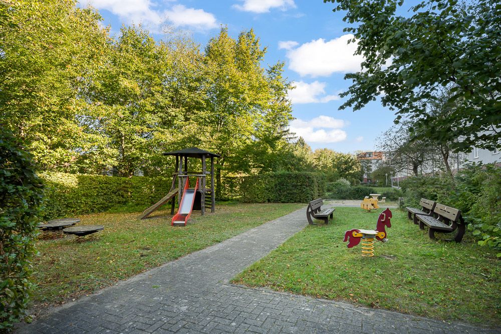 Kleiner Spielplatz im Grünen mit Rutsche, Wipptieren und Bänken.