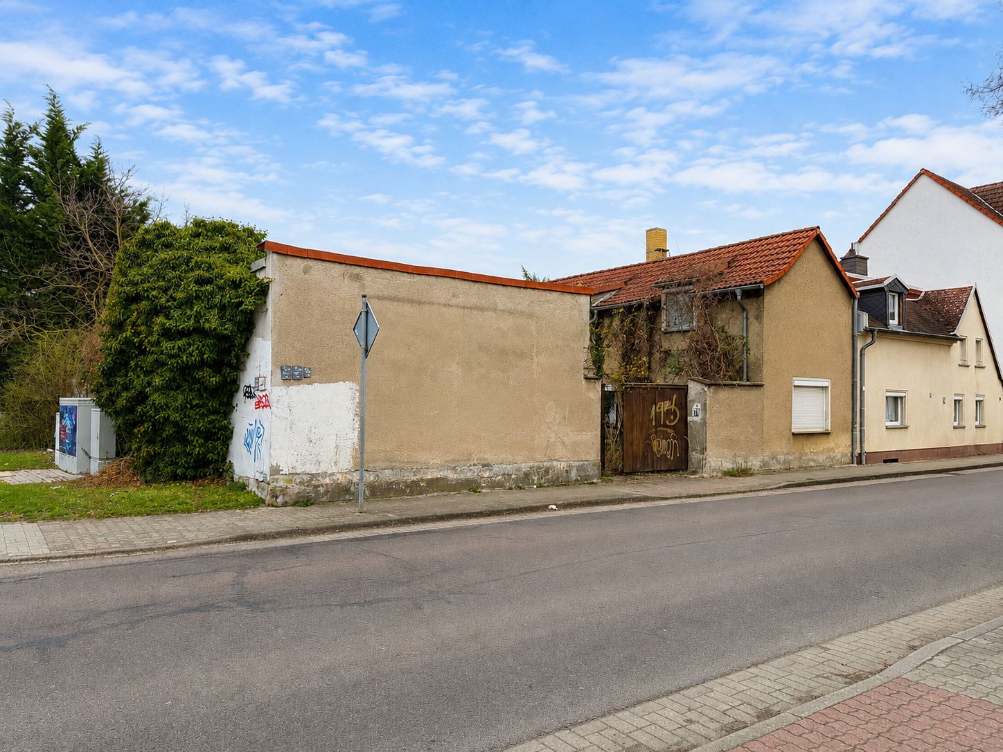 Straßenansicht eines älteren Wohnhauses mit brauner Fassade und rotem Dachziegel.