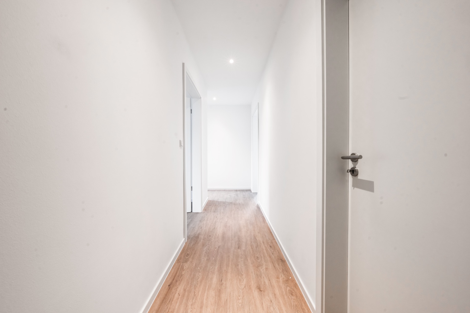 Heller Flur mit Holzfußboden und weißen Wänden in einer Wohnung.