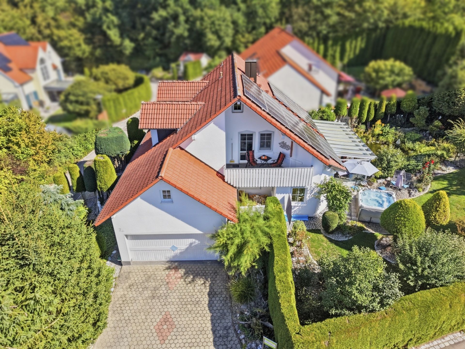 Luftaufnahme eines Einfamilienhauses mit rotem Dach, Garten und Terrasse mit Whirlpool.