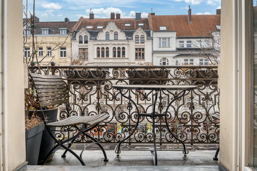 Balkon mit kleinem Tisch und zwei Stühlen, Blick auf Altbaufassaden.