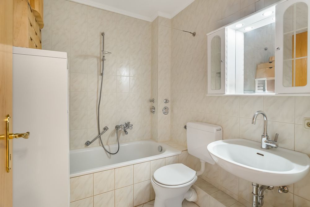 Helles Badezimmer mit Badewanne, Duschkopf, Waschbecken, Spiegel und Toilette.