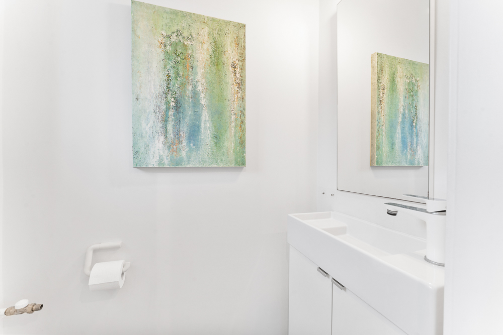 Modernes, weißes Badezimmer mit abstraktem Gemälde, Waschbecken und Spiegel.