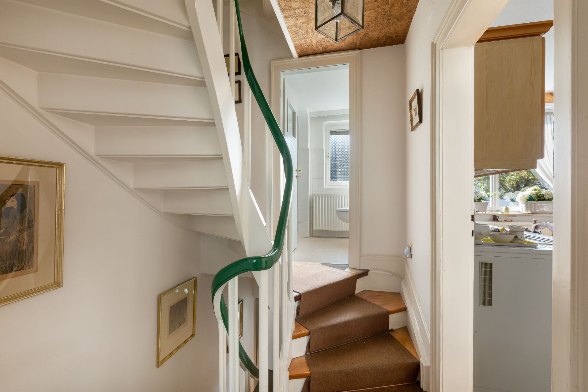 Flur mit Treppe, Zugang zu einem Badezimmer und Blick in eine helle Küche.