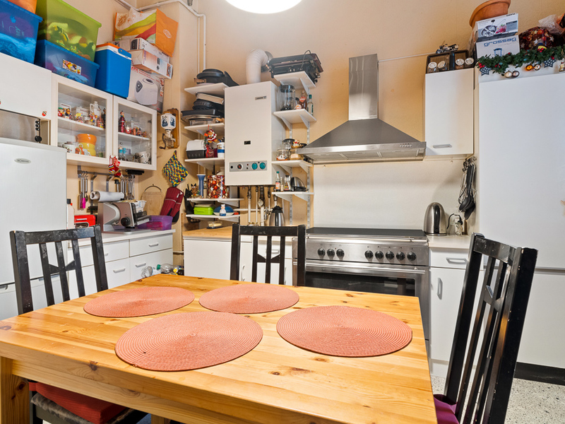 Küche mit Holztisch, vier Stühlen, Herd, Kühlschrank und offenen Regalen mit Haushaltsgegenständen.