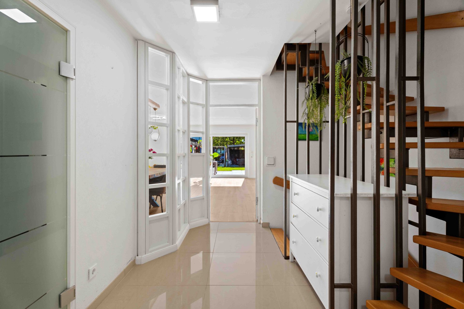 Heller Flur mit Treppe, weißen Wänden, Schrank, Glastür und Blick nach draußen.