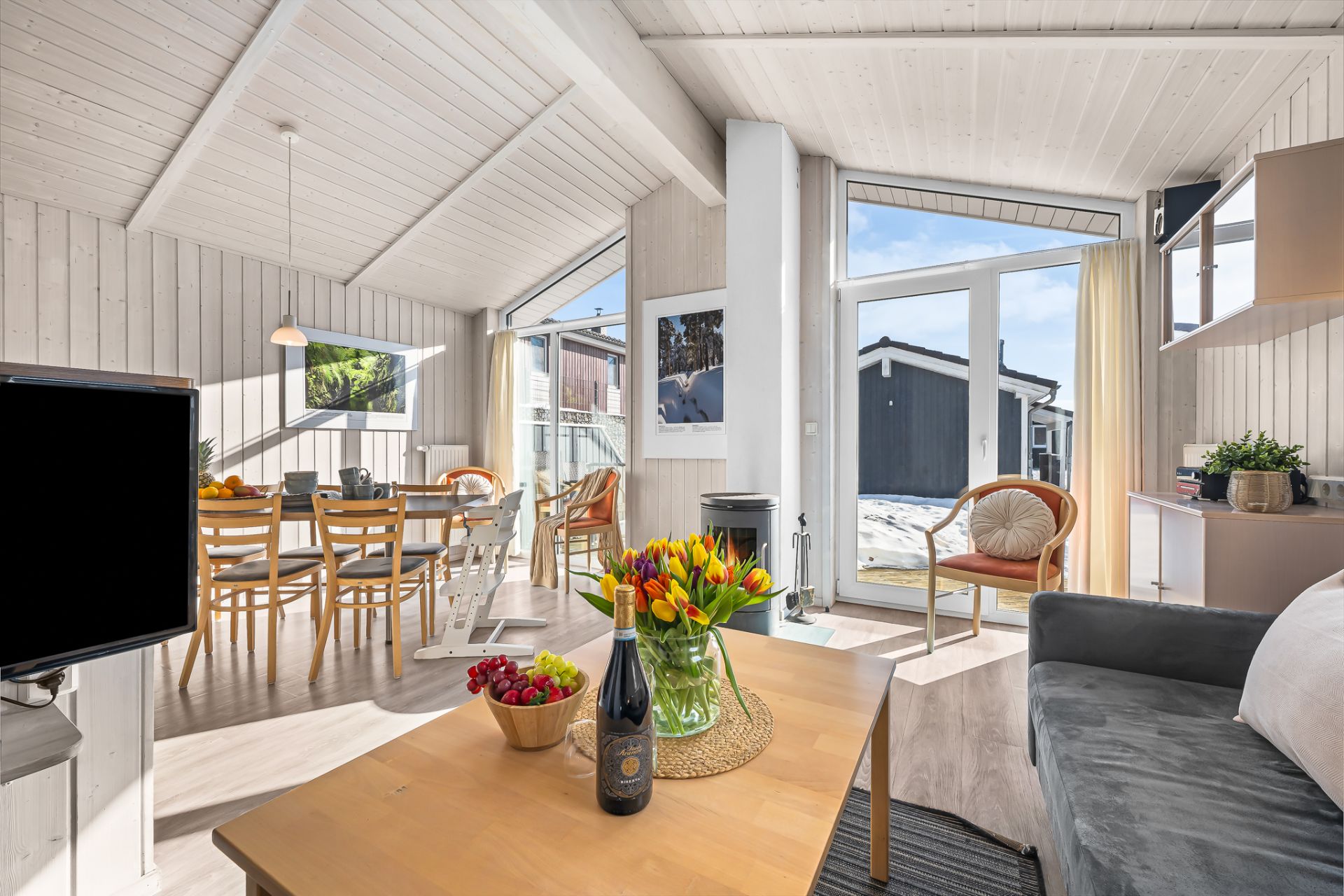 Helles Wohnzimmer mit Esstisch, Sofa, Blumen auf dem Tisch und großen Fenstern zum Garten.