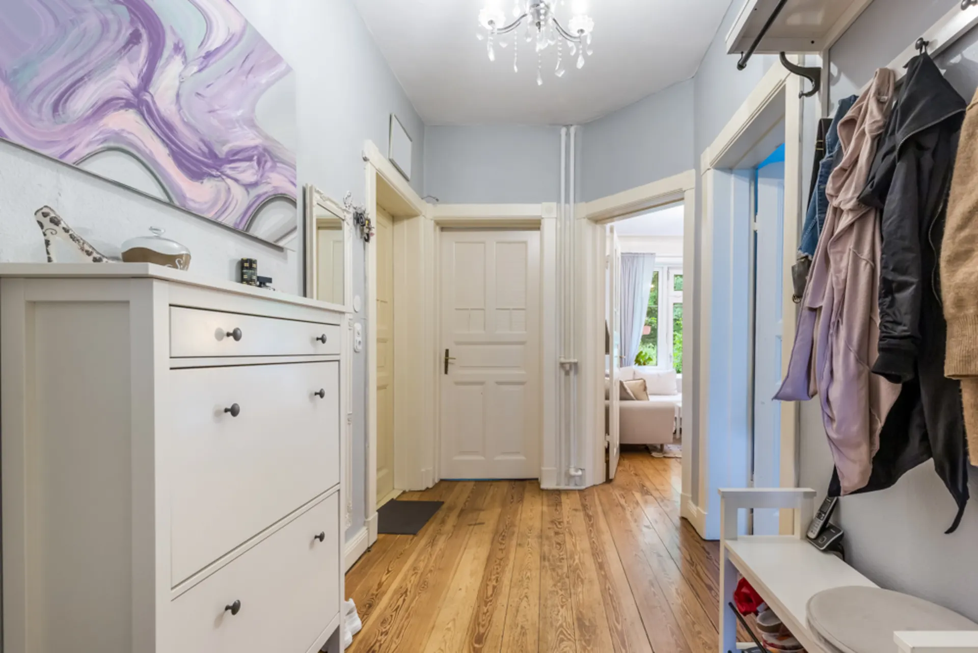 Heller Flur mit Holzfußboden, weißem Schuhschrank, Garderobe und offenem Durchgang zum Wohnzimmer.