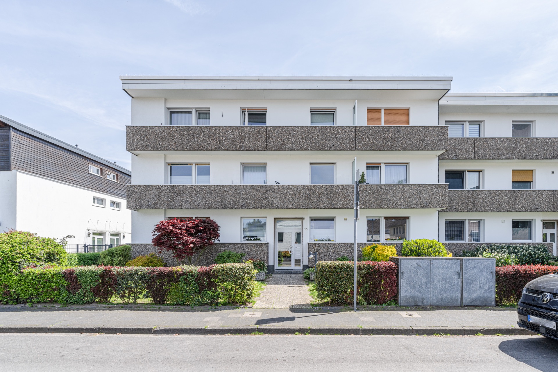 Dreistöckiges Wohnhaus mit Balkonen und Vorgarten, an einer ruhigen Straße gelegen.