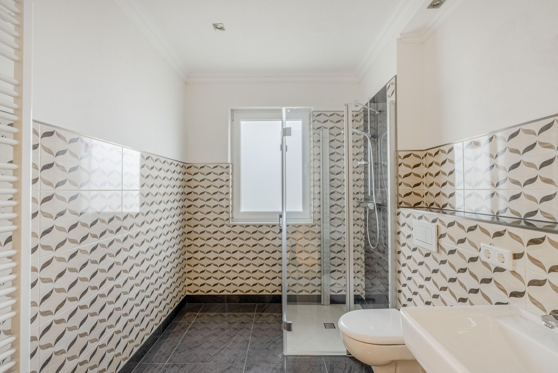 Modernes Bad mit gemusterten Fliesen, Dusche, Waschbecken und Fenster.
