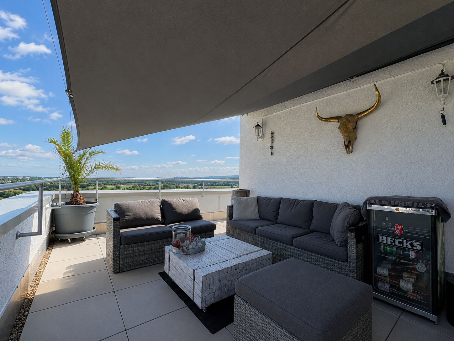Moderne Terrasse mit Sitzgruppe, Sonnenschutz, Pflanze im Topf und Deko an der Wand.