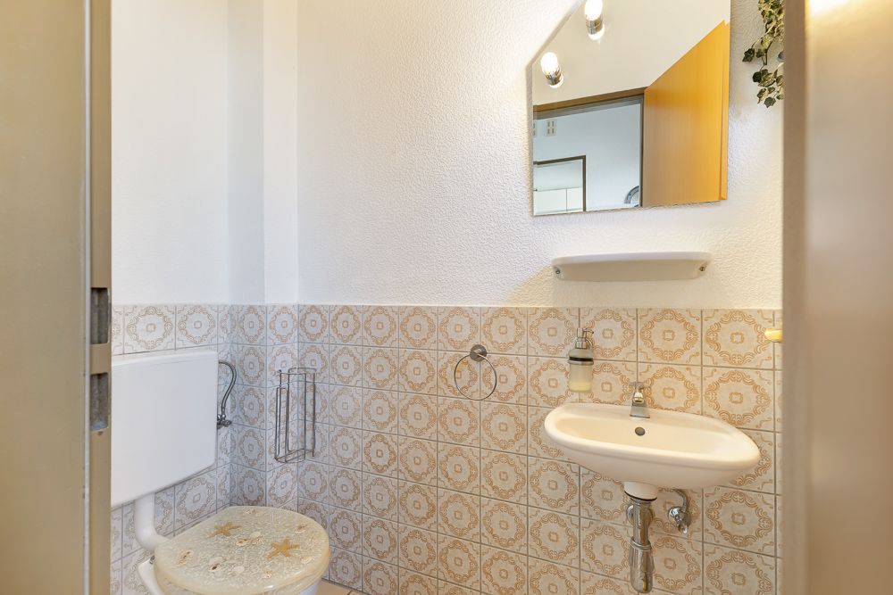 Kleines Badezimmer mit WC, Waschbecken, Spiegel und gemusterten Fliesen.