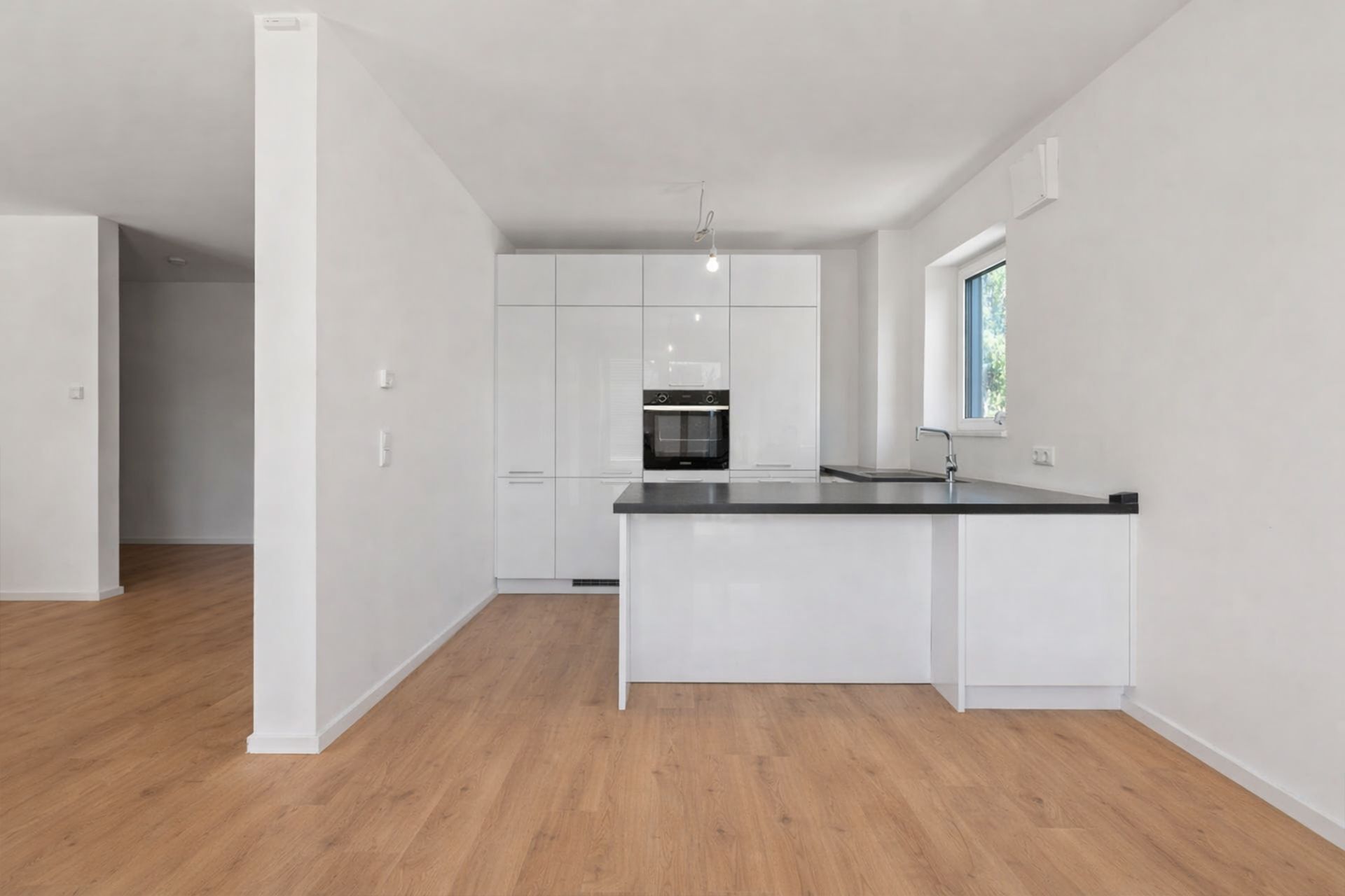 Moderne weiße Einbauküche mit Kochinsel, Holzfußboden und Fenster.