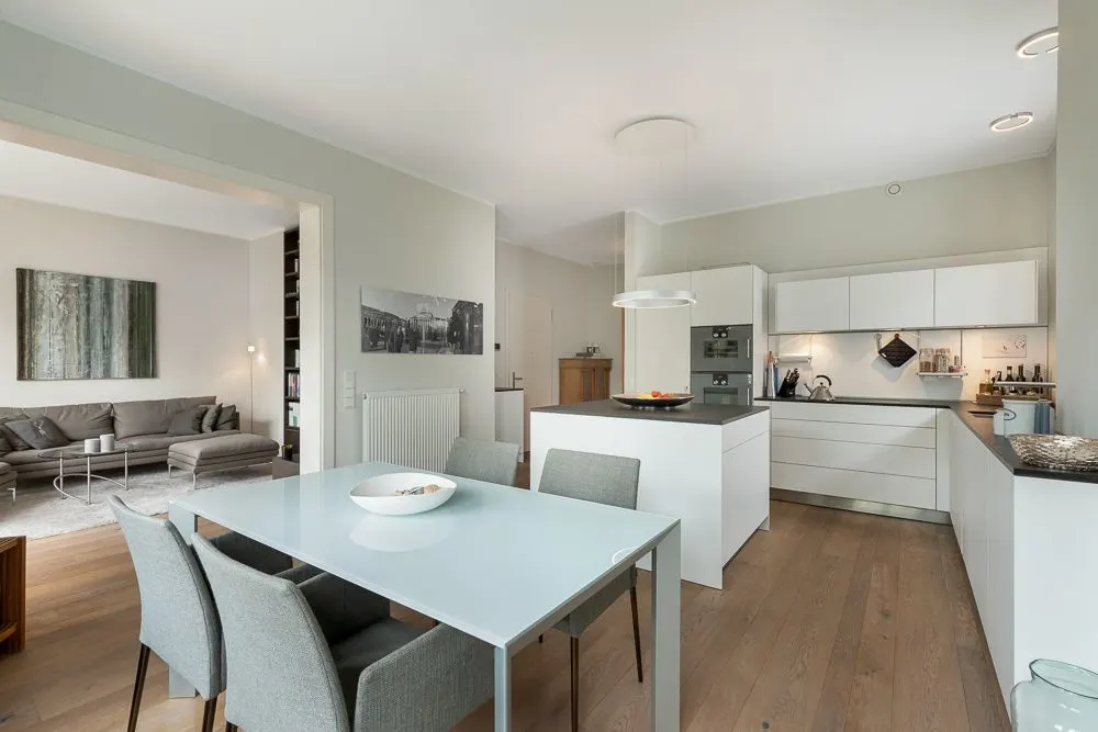 Moderne offene Küche mit Essbereich und Blick ins Wohnzimmer mit grauem Sofa.