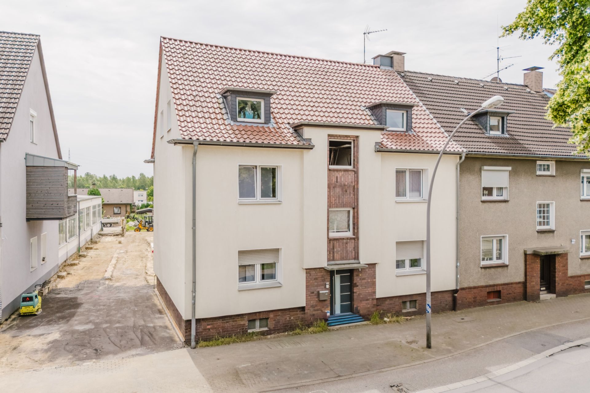 Dreistöckiges Wohnhaus mit Satteldach und mehreren Fenstern, davor eine Straße.