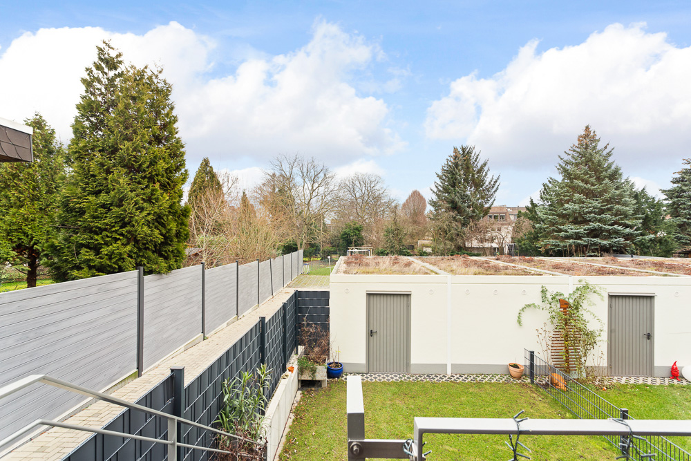 Blick auf Garten, Rasenfläche, weiße Garage mit Türen und hohe Bäume im Hintergrund.