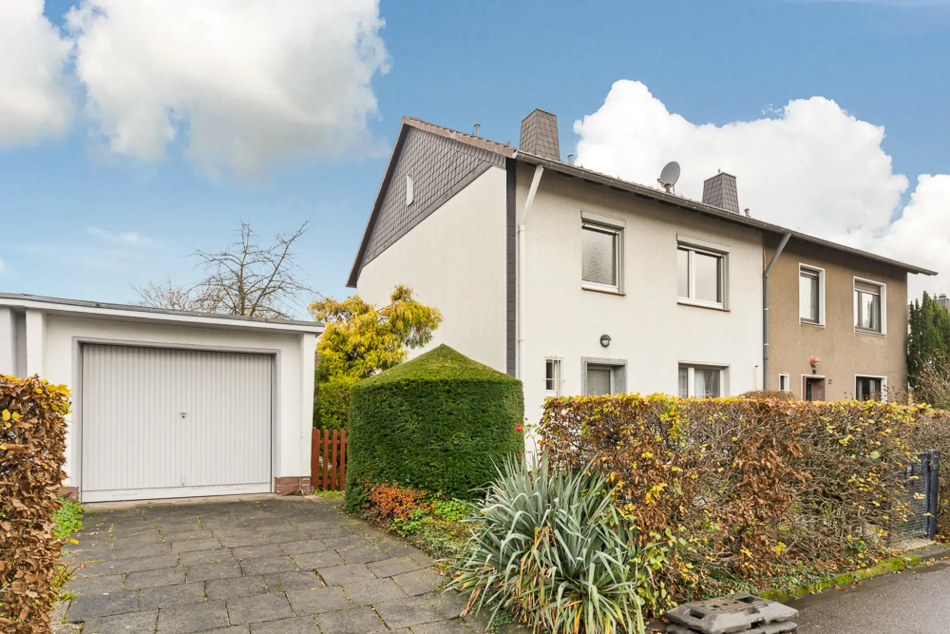 Zweistöckiges Reihenhaus mit Garage, Hecke und bepflanztem Vorgarten bei Tageslicht.